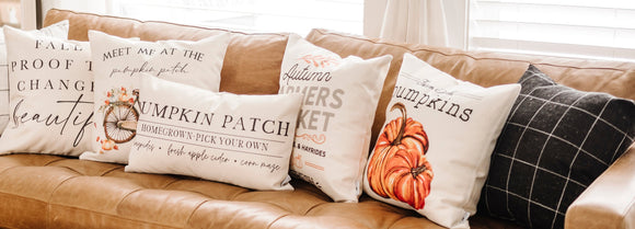 Brown leather sofa with decorative pillows featuring autumn-themed designs in a living room.