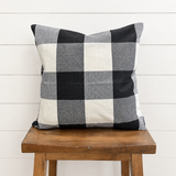 Black and white large buffalo-check pillow cover displayed on a wooden stool against a white shiplap wall.